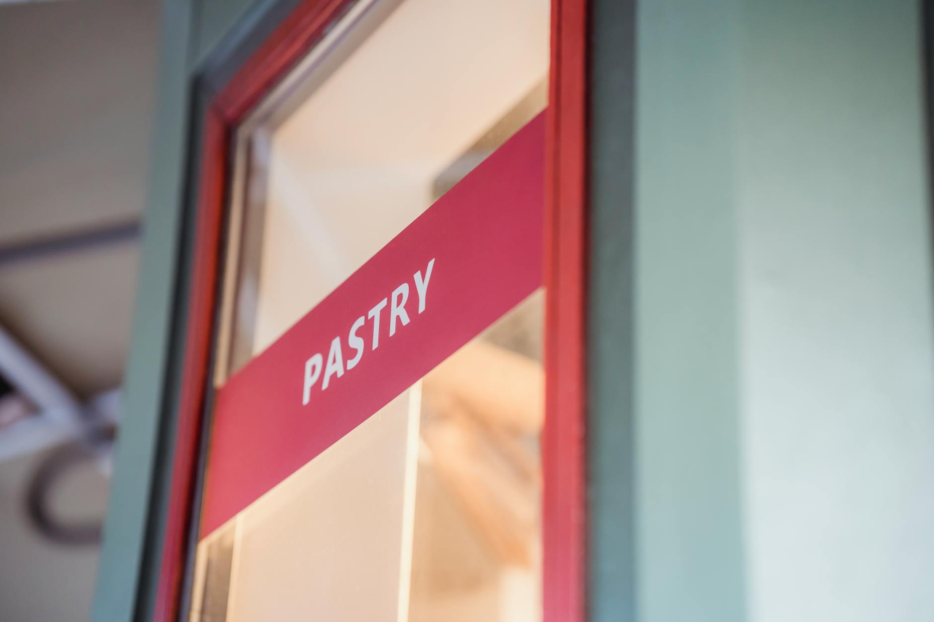 Close-up of a modern pastry shop sign with red accents, emphasizing dessert offerings.