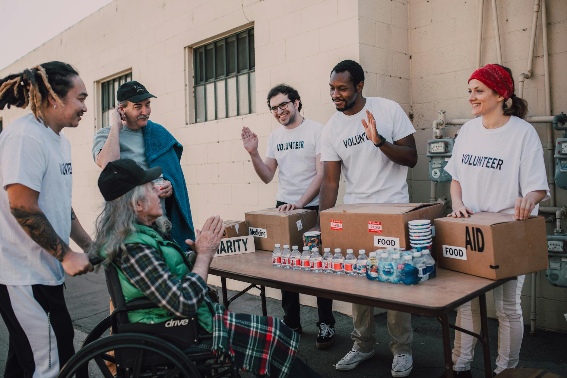 Group of volunteers providing food and aid to a person in wheelchair outdoors.